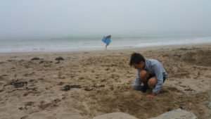 Kind buddelt bei Regen am Strand